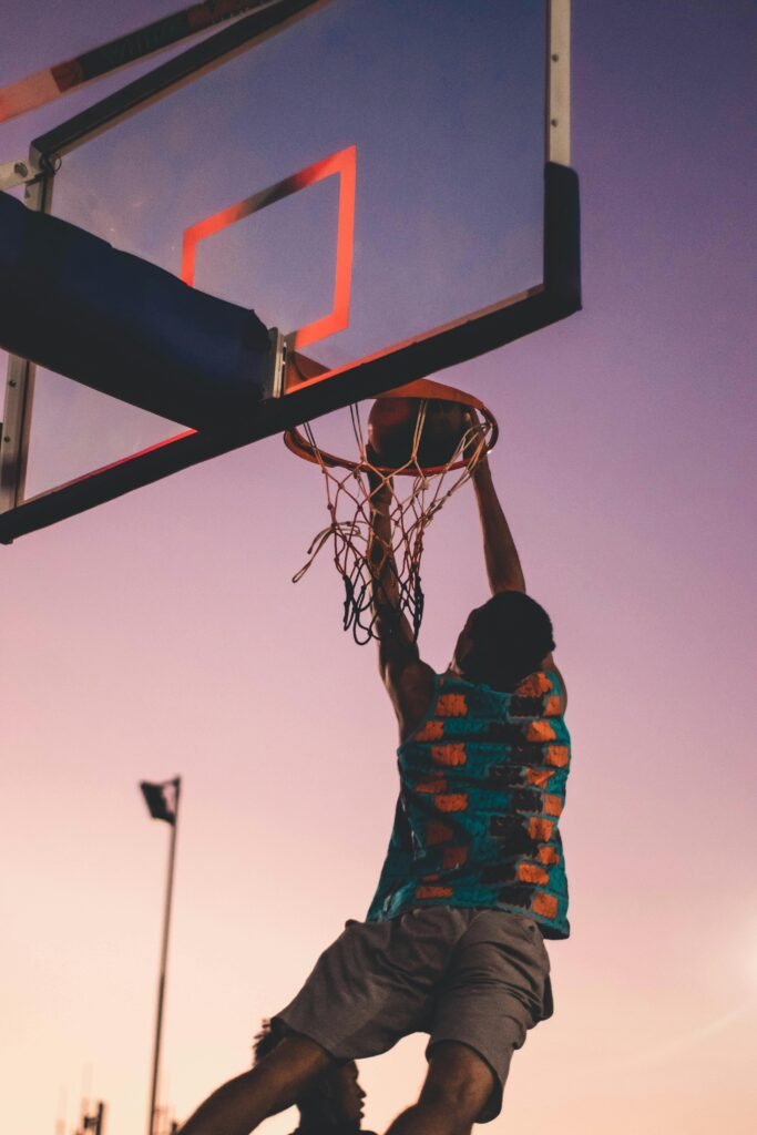 Categories A basketball player successfully dunks as the sun sets, creating a dramatic silhouette.