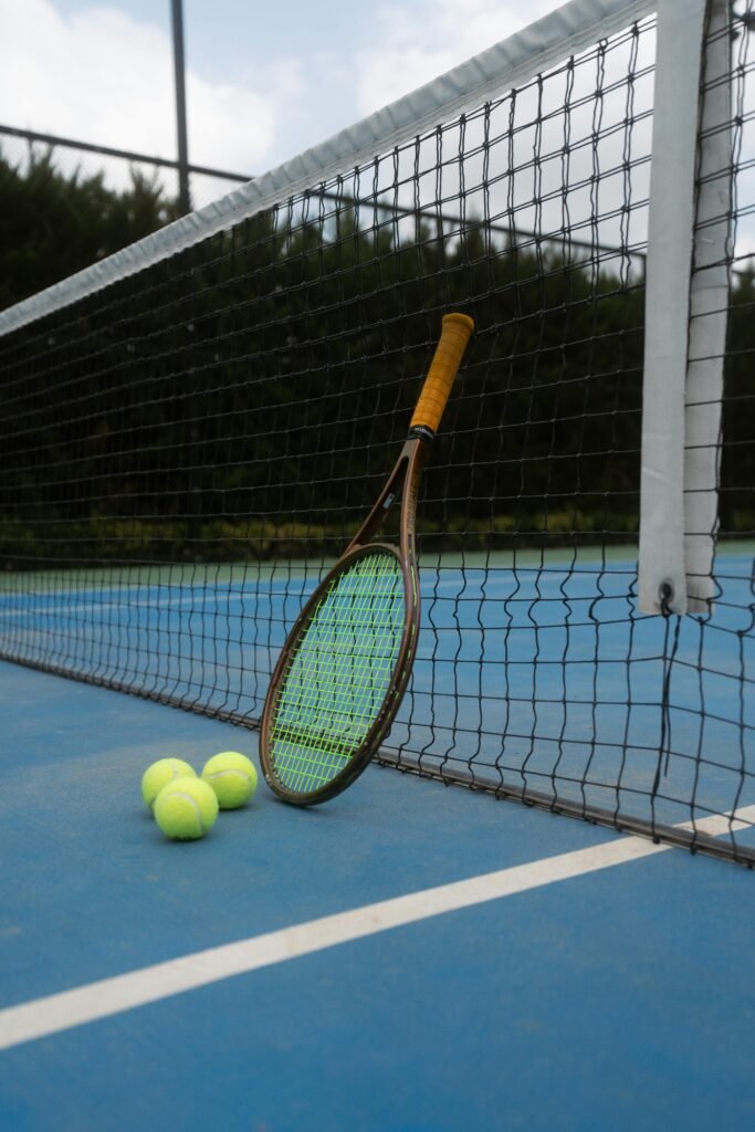 Categories A vintage tennis racket and balls on an outdoor blue court, perfect for sports enthusiasts.